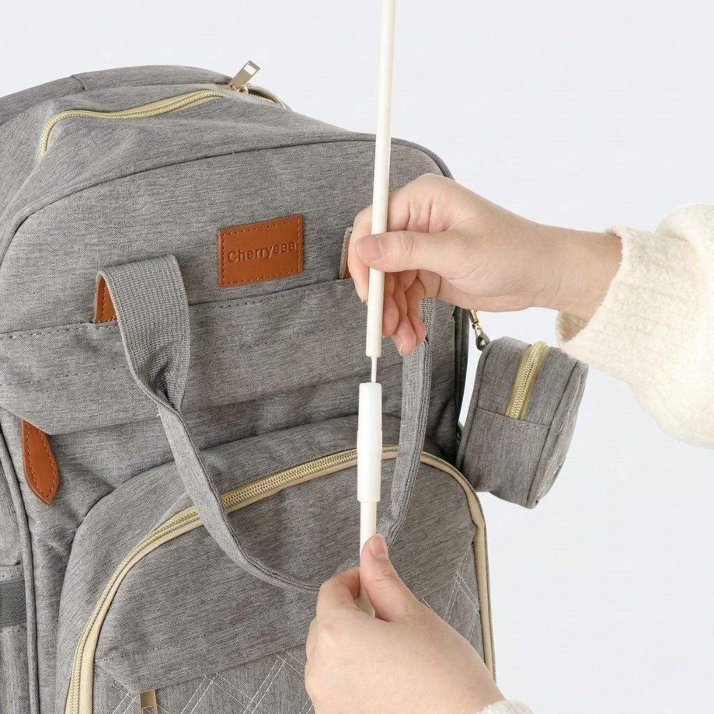 Mains assemblant l'arche de jeux du lit pliable du sac à langer gris chiné, tiges blanches à emboîter