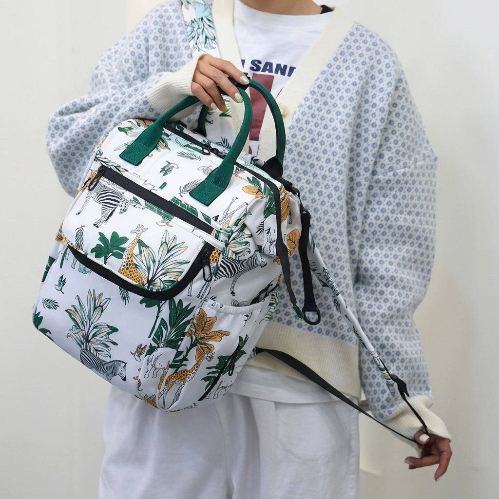 Sac à dos à langer blanc safari porté à la main par une femme, anses vertes et format compact