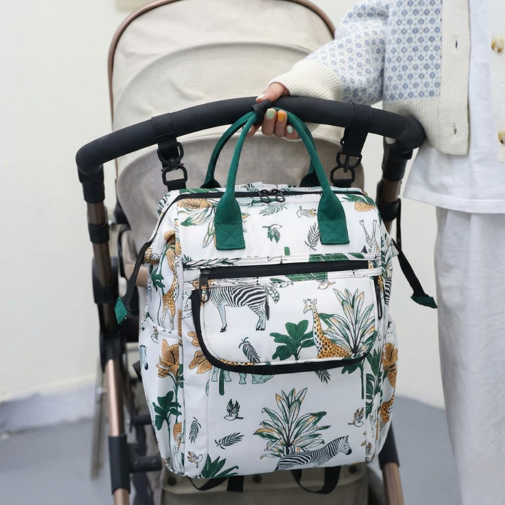 Sac à dos à langer blanc imprimé girafes et feuilles tropicales, accroché à une poussette par une femme Image