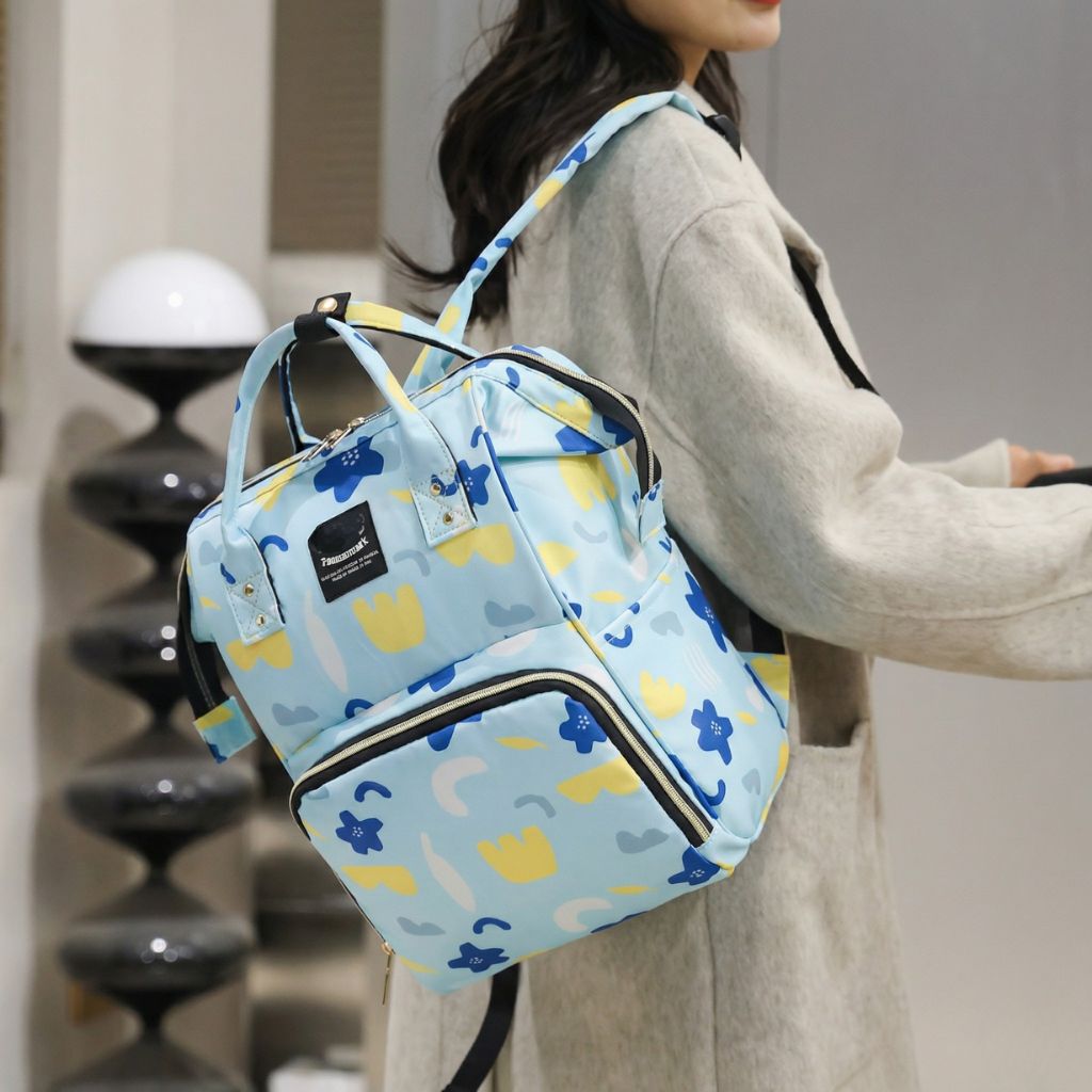 Sac à dos à langer bleu ciel fleurs colorées porté en épaule par une femme de profil, sortie bébé