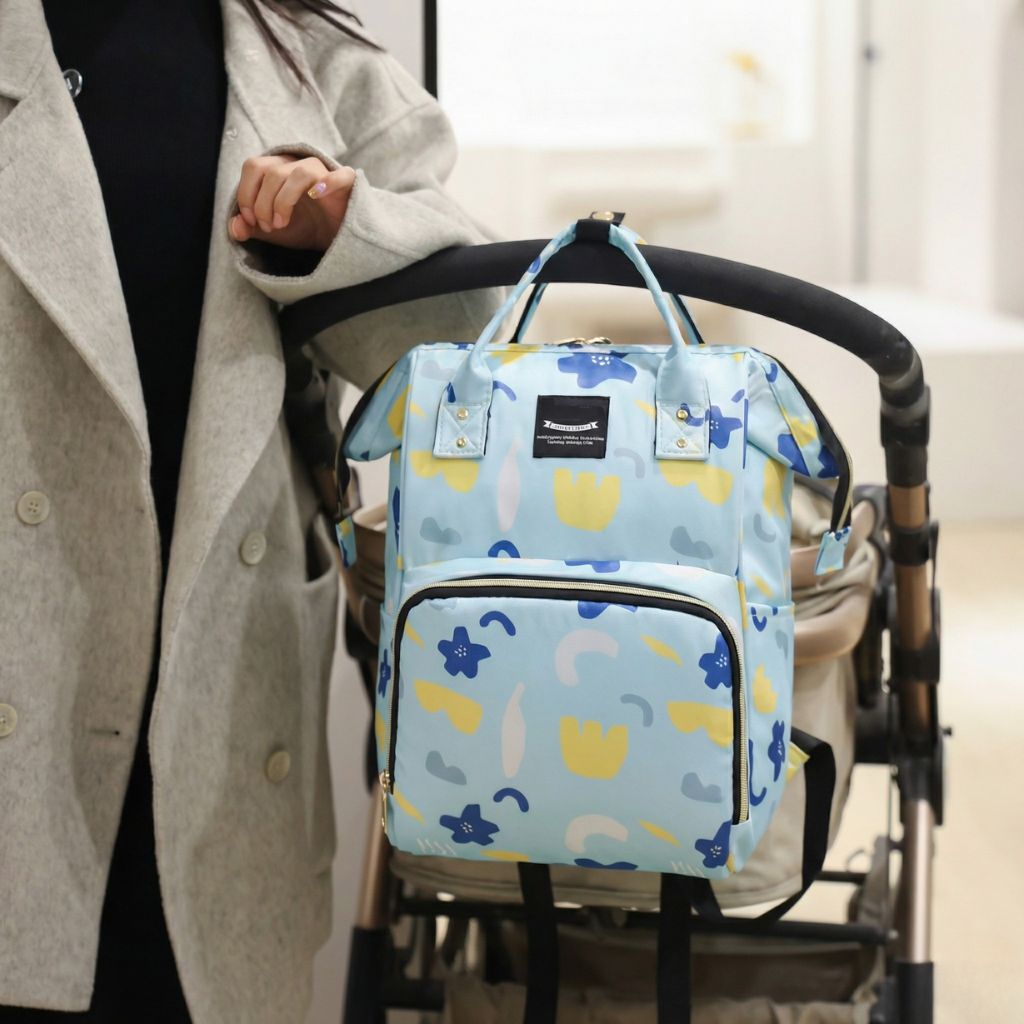 Sac à dos à langer bleu à fleurs jaunes et bleues accroché à une poussette, tenu par une femme en manteau beige Image