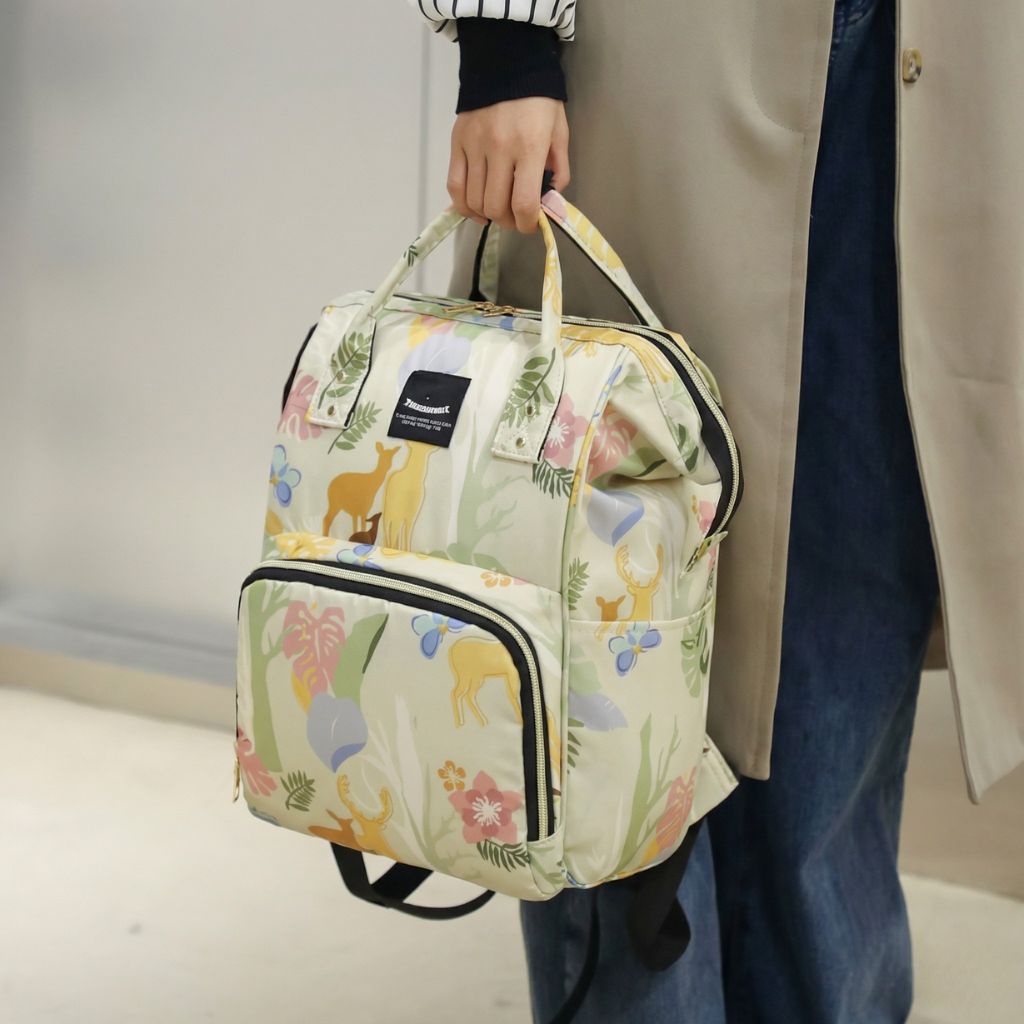 Sac à dos à langer beige crème motif biche porté à la main par une femme en balade avec bébé