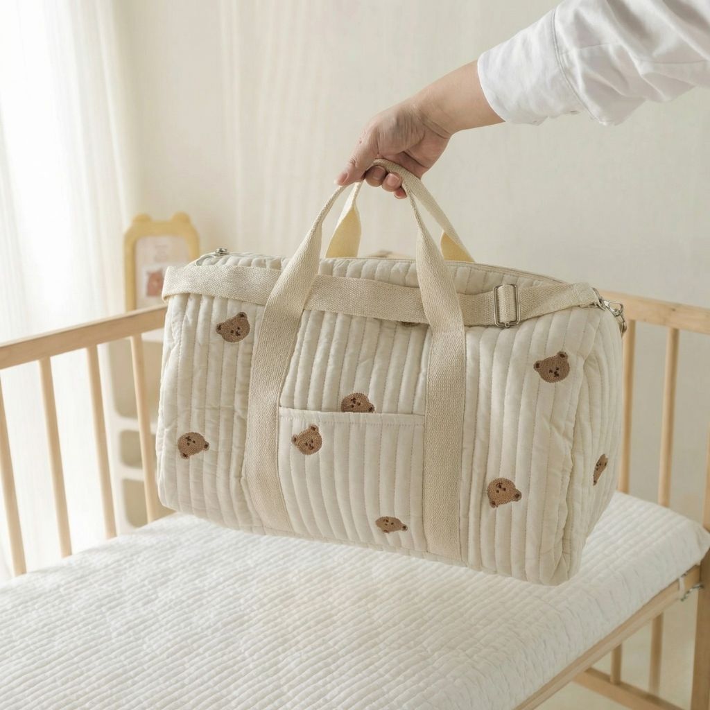 Sac à langer matelassé crème à ours brodés tenu par la poignée devant un lit de bébé en bois