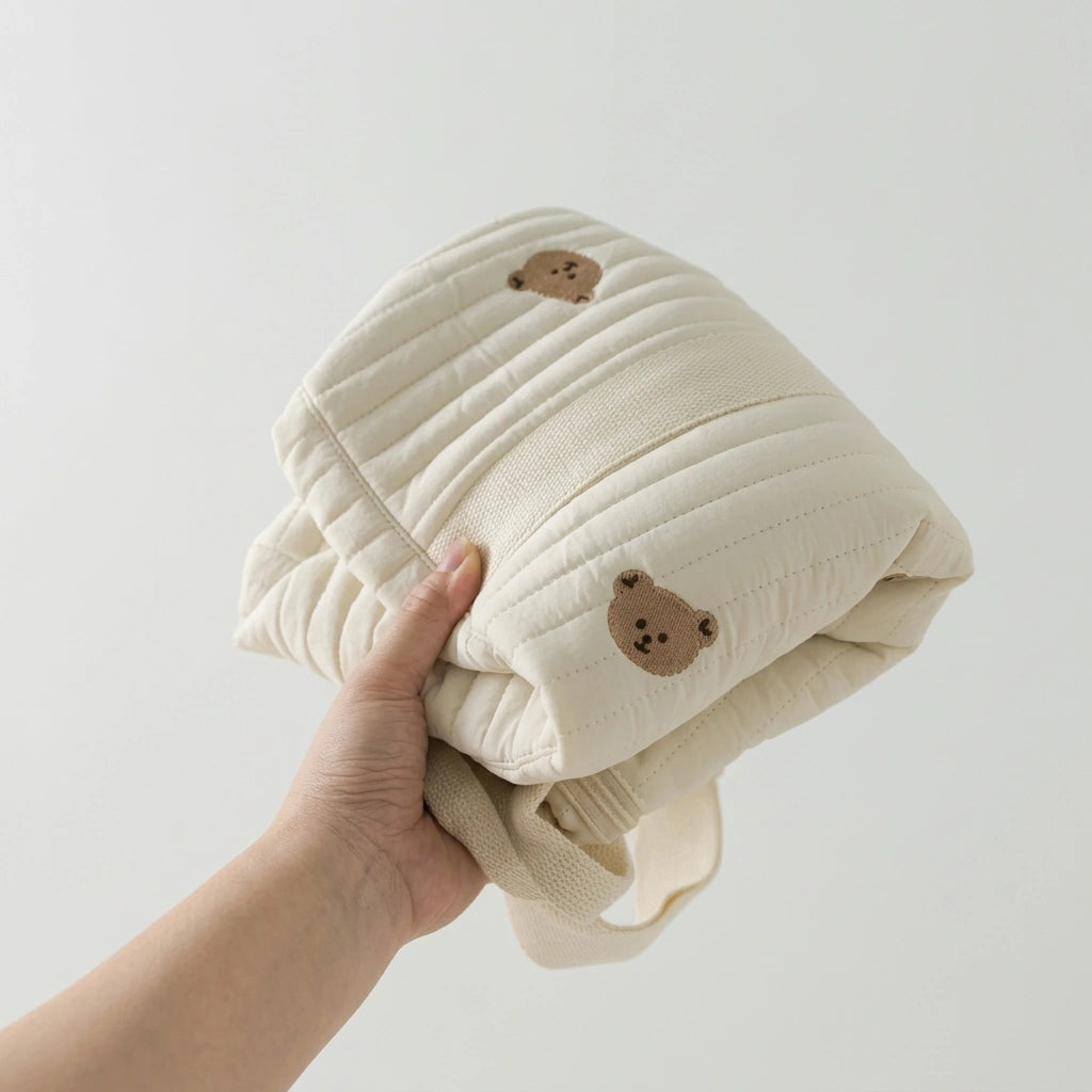Sac à langer matelassé ourson compressible tenu à la main, démontrant la légèreté du tissu matelassé
