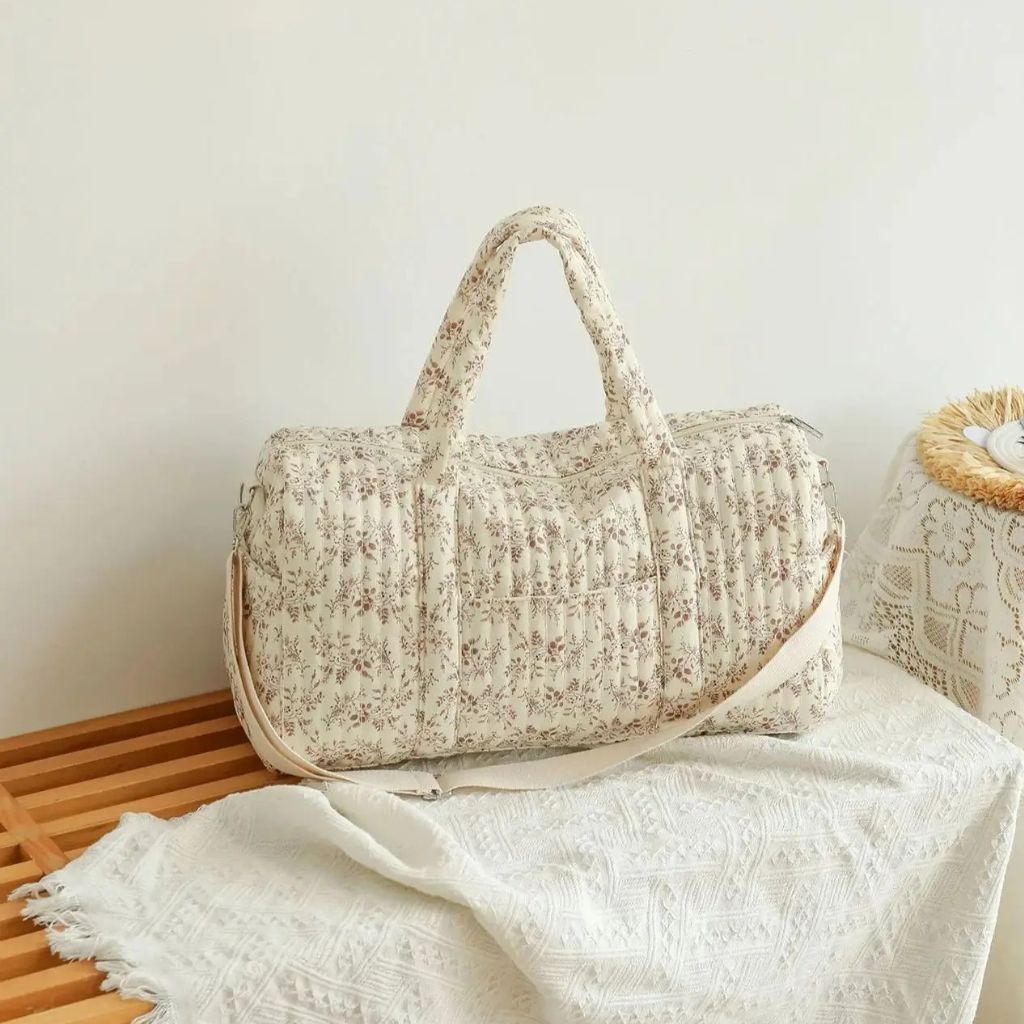 Sac à langer fleuri rose posé sur un banc en bois avec couverture blanche, ambiance maternité cosy