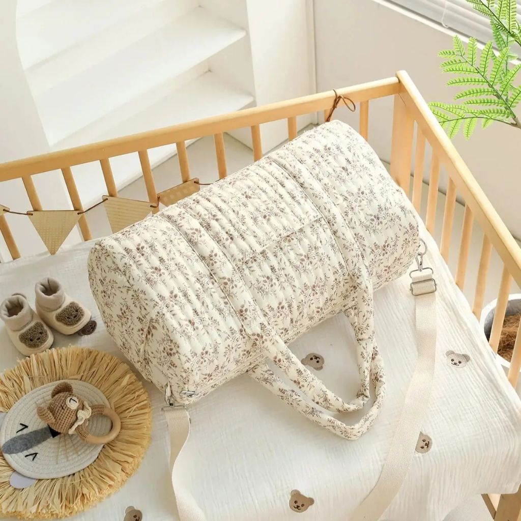 Sac à langer fleuri rose posé dans un lit de bébé, vue du dessus avec hochet, chaussons et accessoires Image