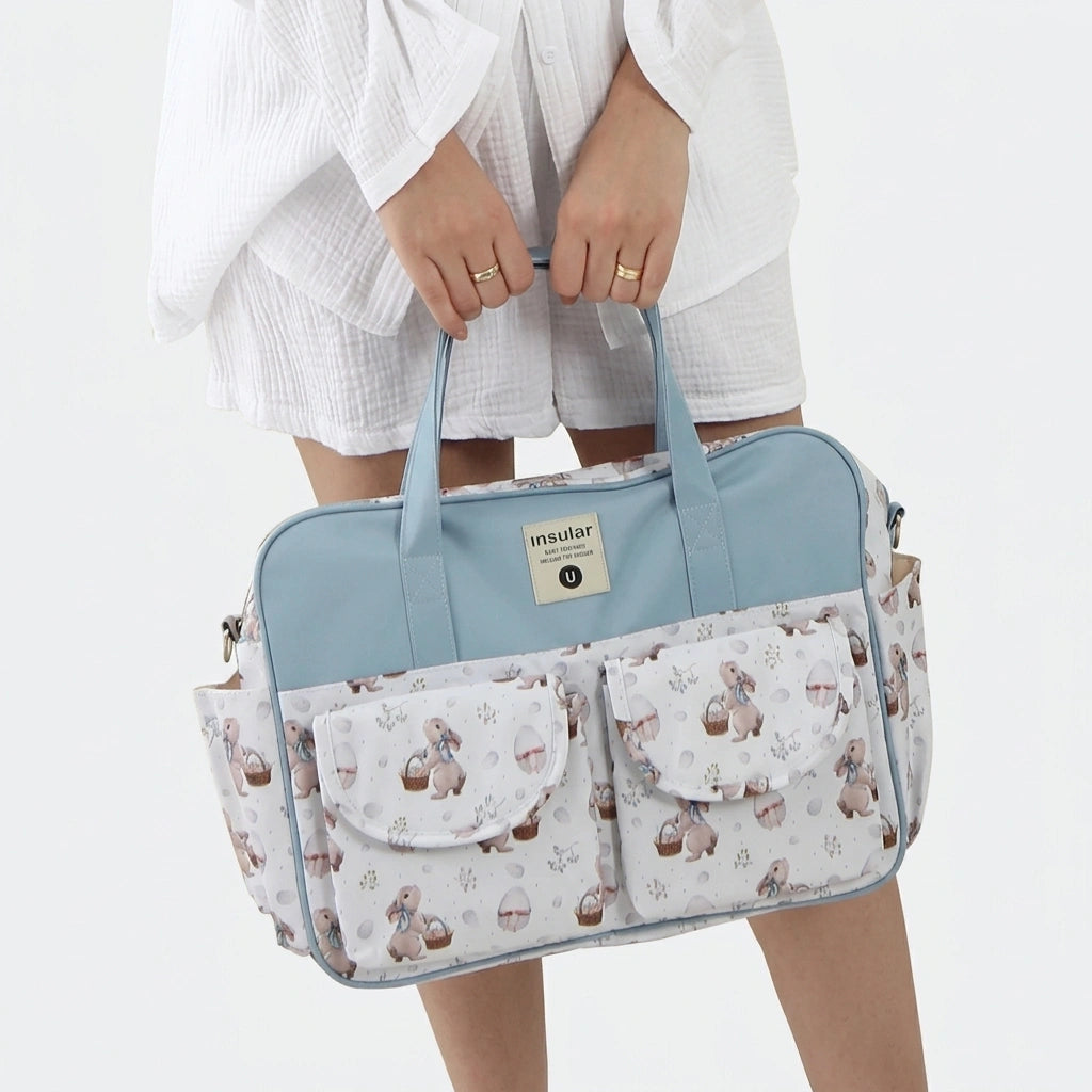Sac à langer cabas bleu ciel motif lapins tenu à deux mains par une femme, format pratique bébé