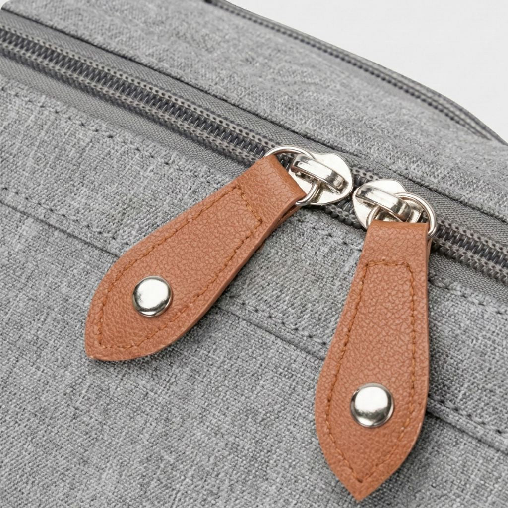 Gros plan des tirettes cuir fauve et de la double fermeture éclair principale du sac gris chiné