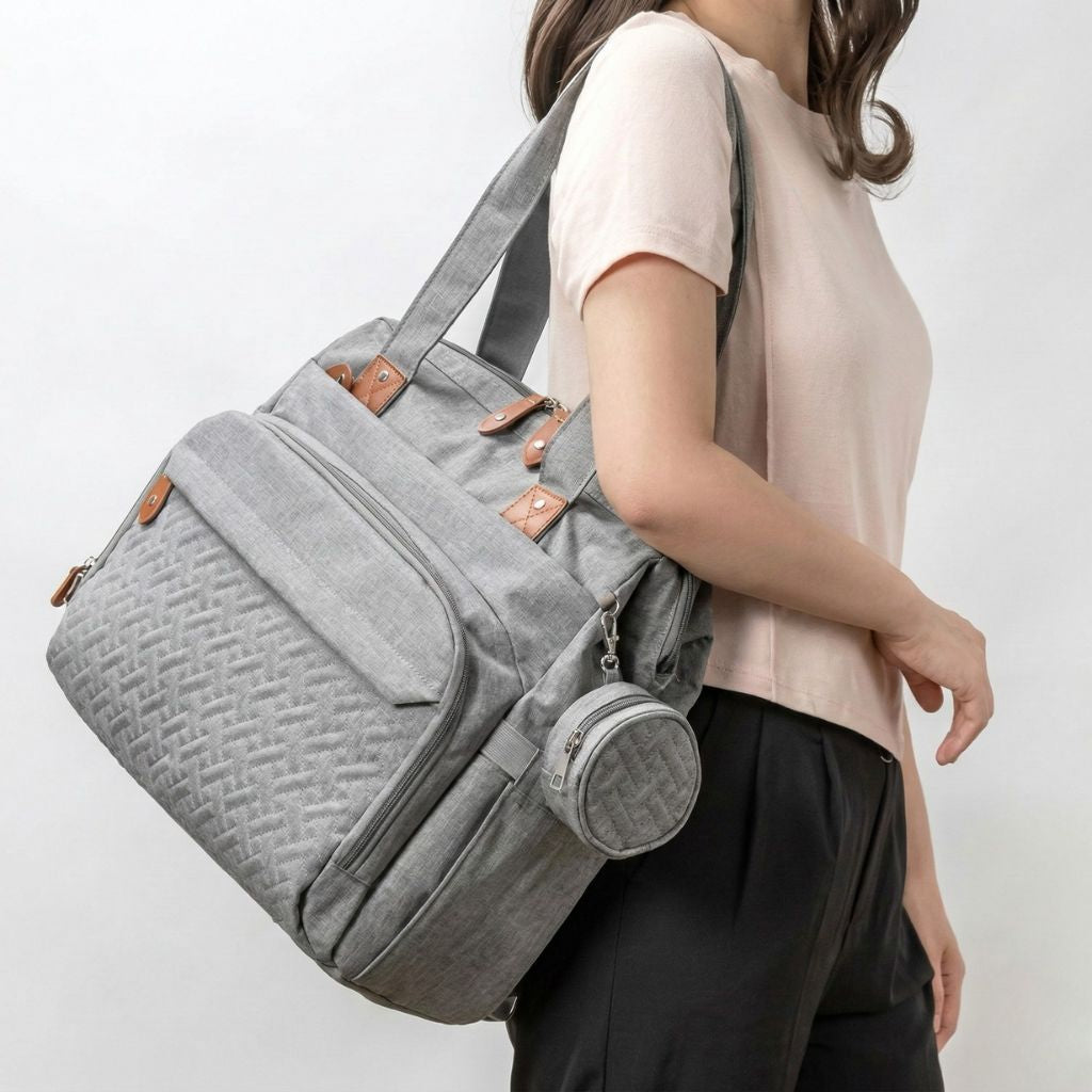 Femme portant sur l'épaule un sac à langer gris chiné, avec bandoulière et petite pochette ronde amovible Image