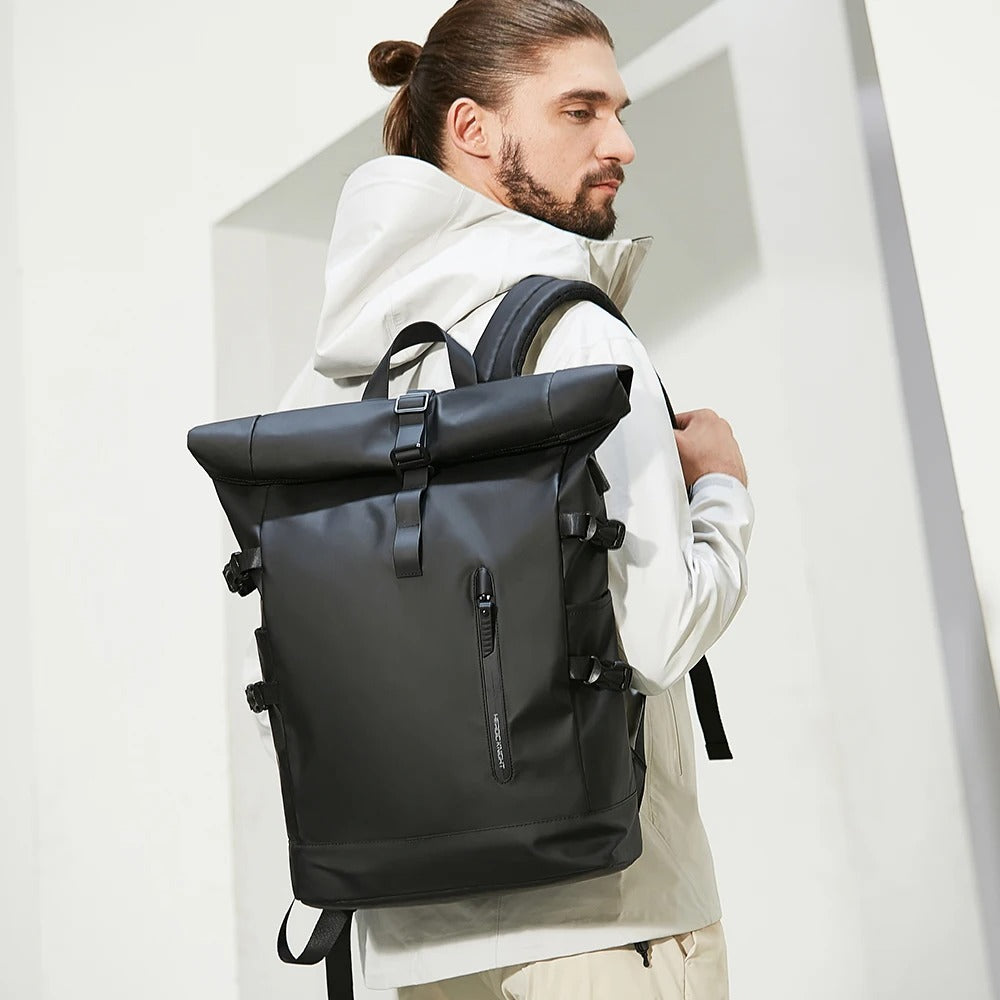Homme portant à la main un sac à dos noir roll-top cabine de voyage, vue de face en extérieur