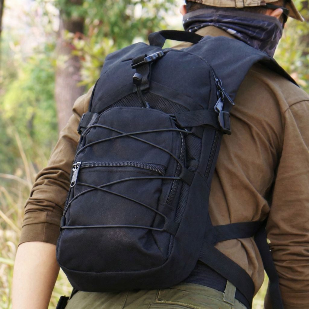 Homme en tenue tactique portant un sac à dos militaire noir compact avec sangles bungee croisées en forêt Image