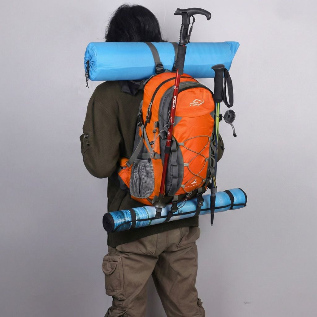 Randonneur de dos portant un sac à dos de randonnée orange avec bâtons de marche et tapis de sol bleu attachés Image