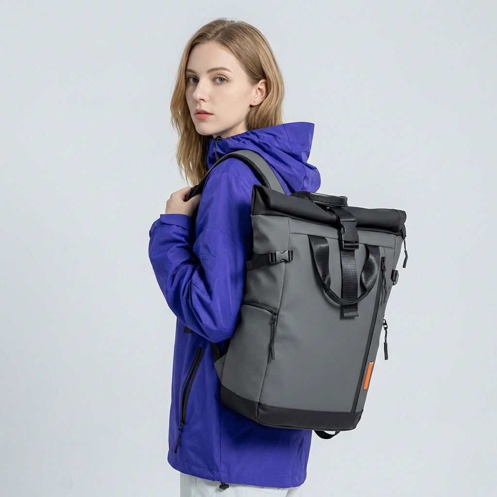 Femme portant un sac à dos voyage roll-top gris de face, bretelles ajustées, veste bleue, languette orange visible