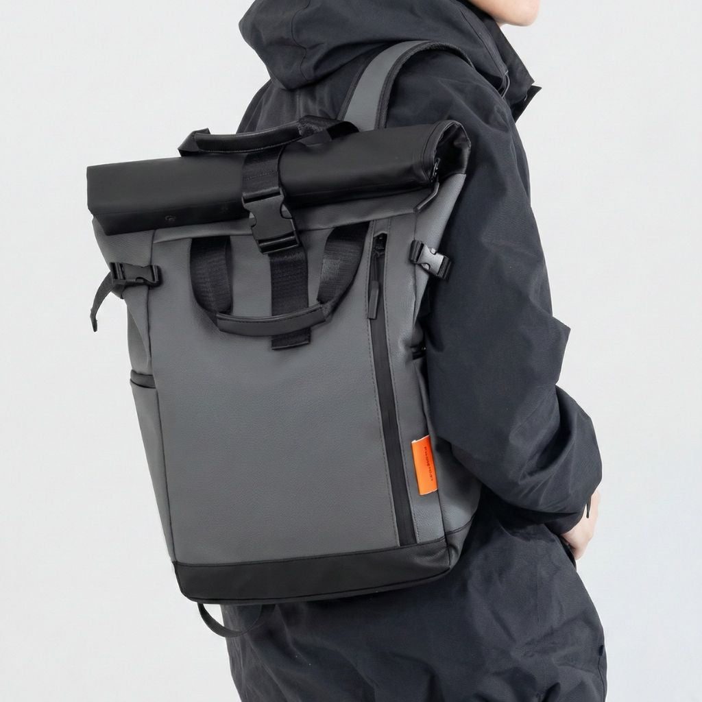Homme de profil portant un sac à dos voyage roll-top gris étanche sous un imperméable sombre, style urbain pratique