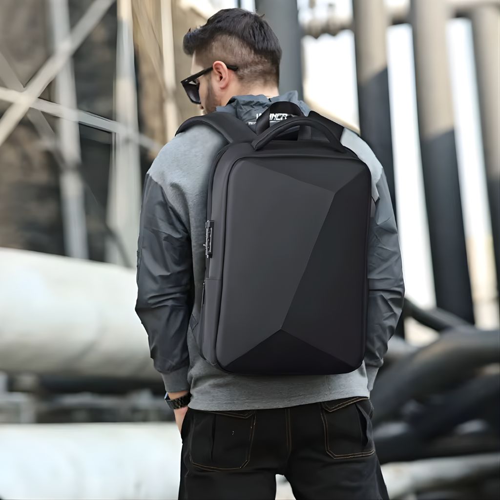 Homme portant un sac à dos à coque noire dans un cadre urbain industriel, vue de dos, bretelles rembourrées