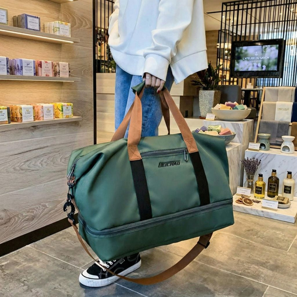 Homme tenant à la main un sac de voyage de sport vert bouteille, poignées caramel, poche chaussures séparée en bas