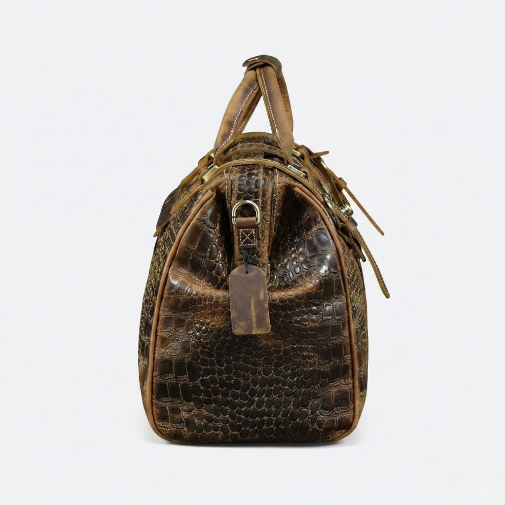 Profil latéral du sac de voyage cuir croco brun, étiquette de bagage en cuir naturel et passant de bandoulière