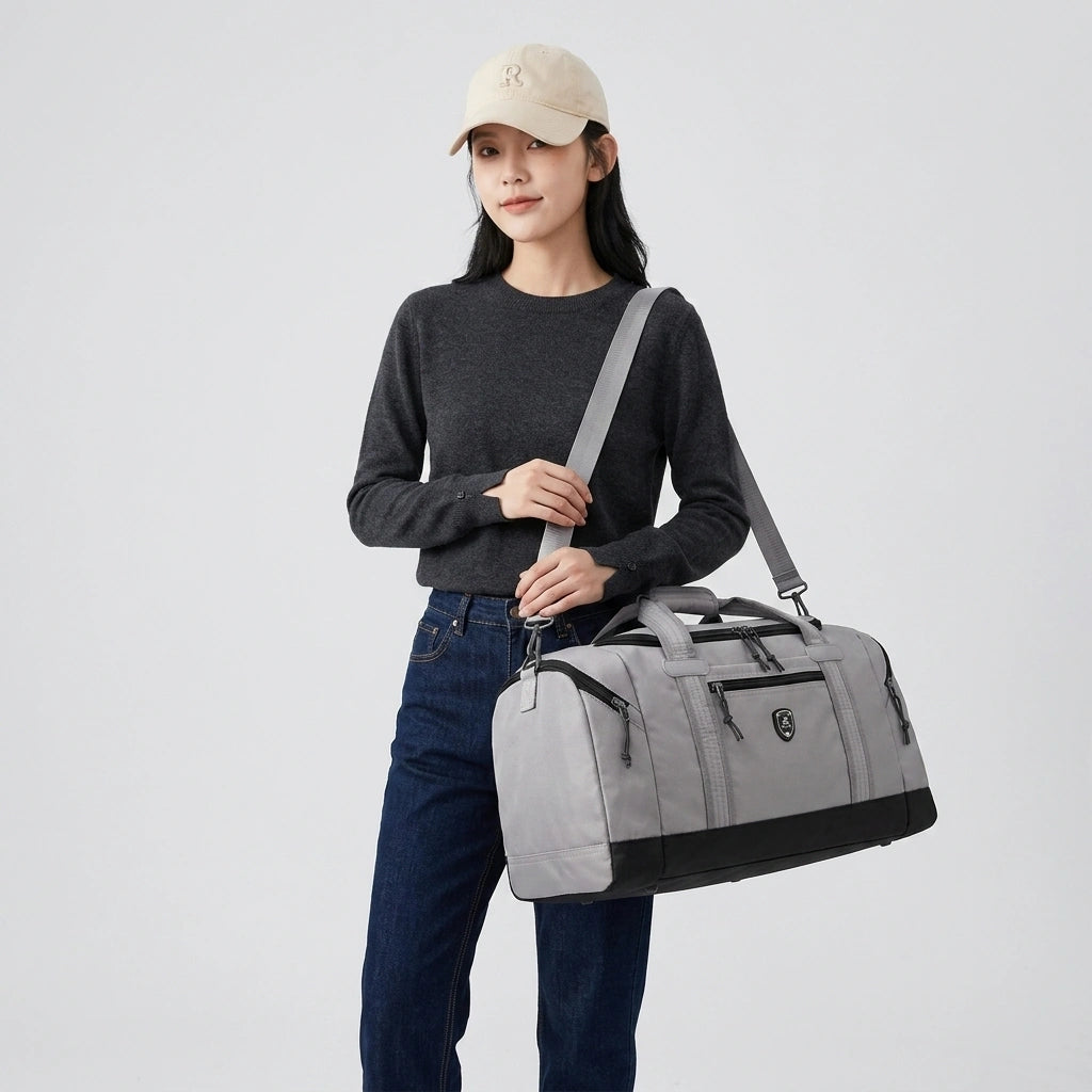Femme en casquette beige et pull gris portant un sac de voyage gris en bandoulière, fond blanc