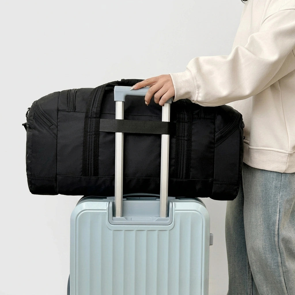 Femme en sweat blanc posant un sac de voyage noir sur la poignée d'une valise bleue grâce au passant trolley