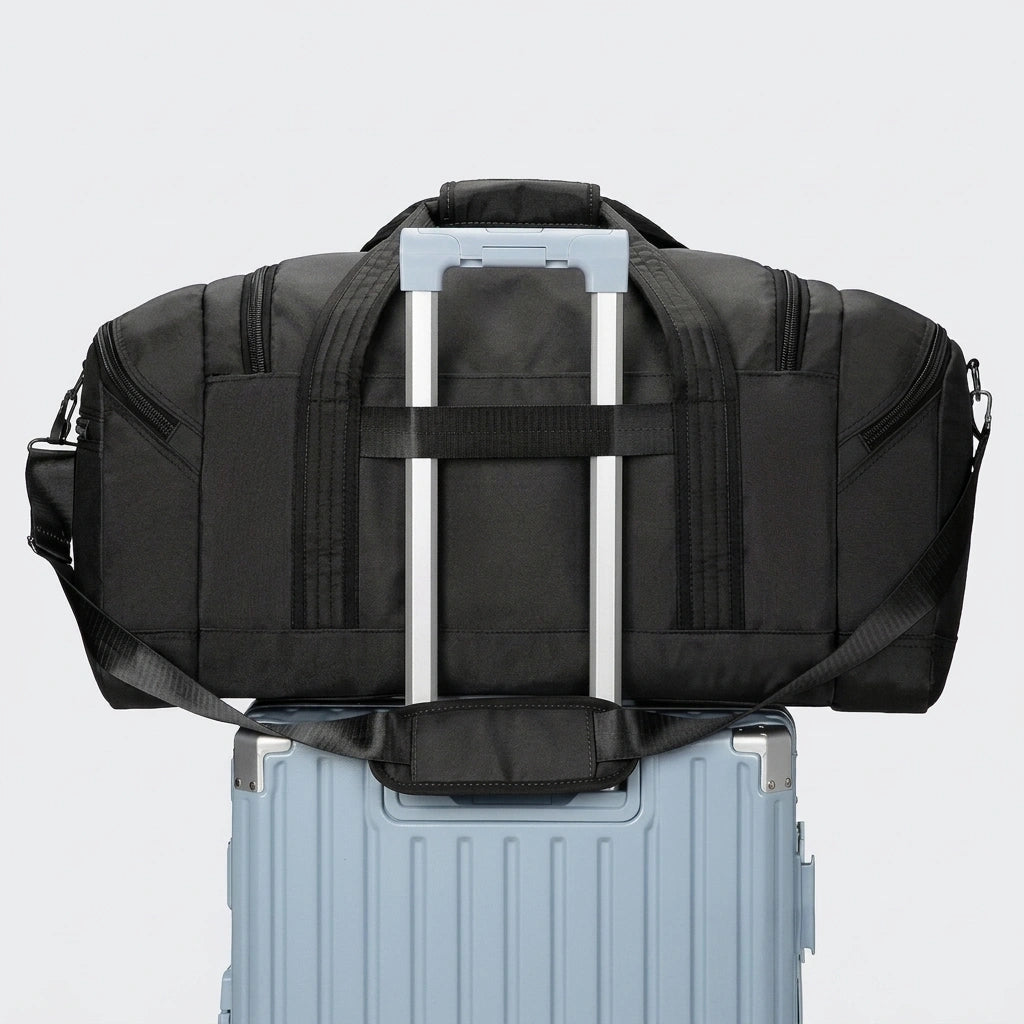 Sac de voyage noir fixé sur la poignée d'une valise à roulettes bleue grâce au passant trolley intégré