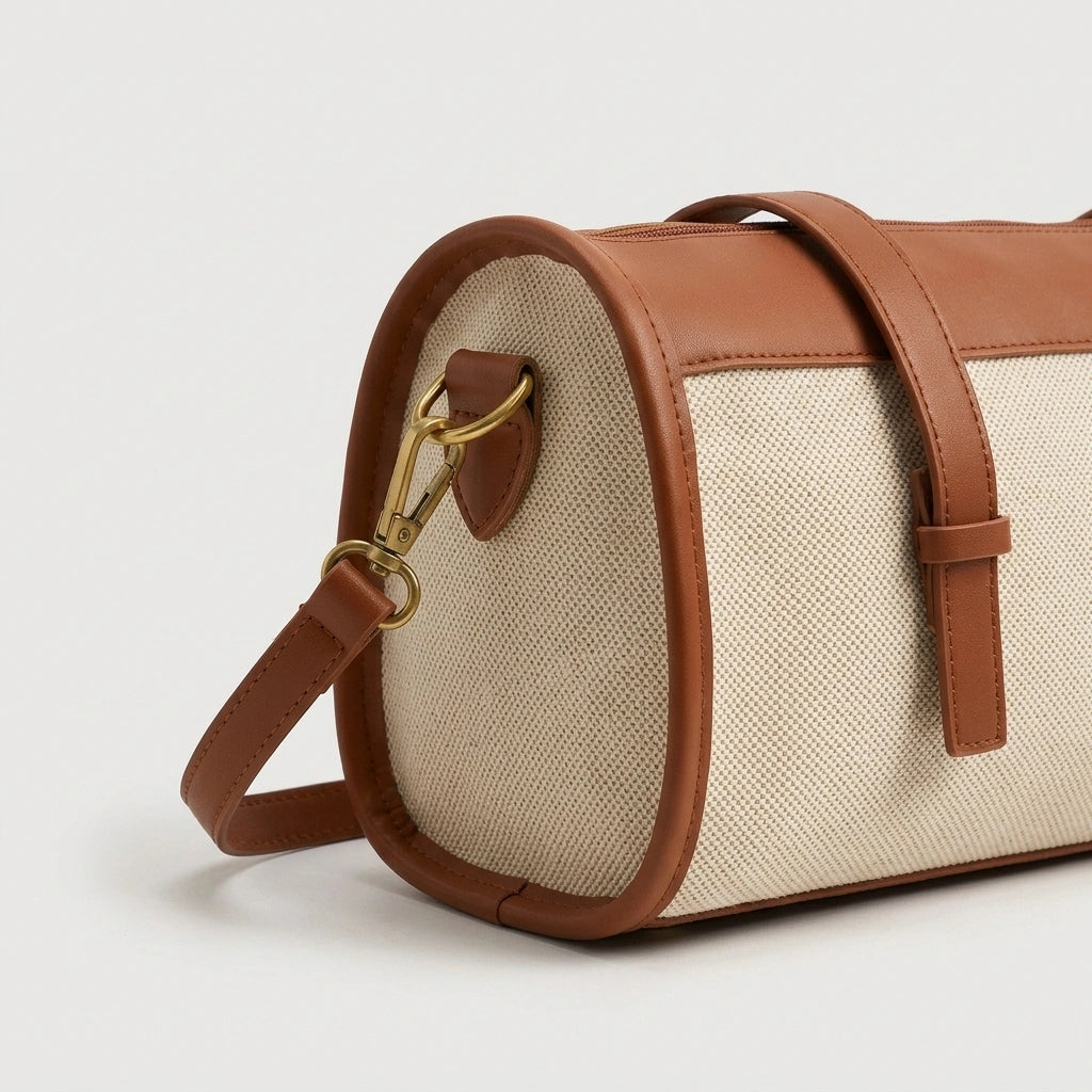 Gros plan sur la fixation de la bandoulière d'un sac de voyage vintage camel, mousqueton doré et toile beige