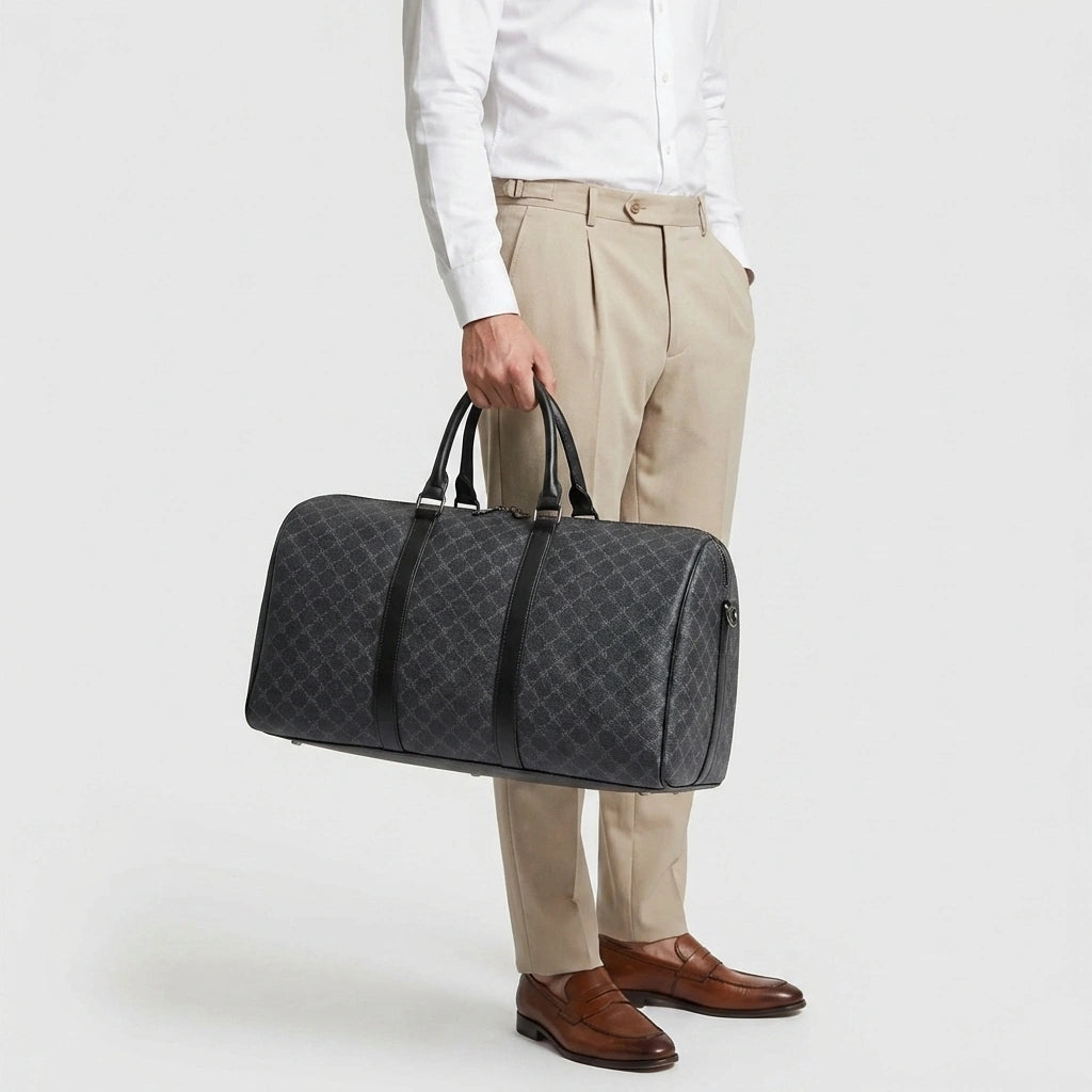 Sac de voyage homme gris damier tenu à la main, vue de côté, mannequin en chemise blanche et pantalon sable