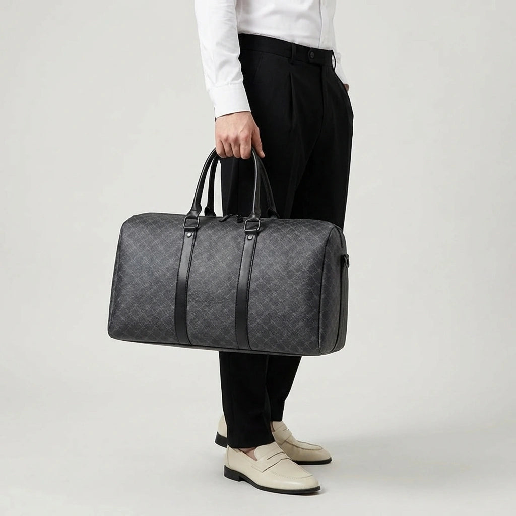 Sac de voyage homme gris foncé damier porté à la main, mannequin en chemise blanche et pantalon noir, vue de face