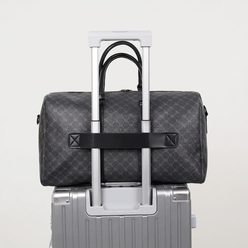 Sac de voyage homme gris damier posé sur une valise cabine argentée grâce à la sangle trolley intégrée à l'arrière