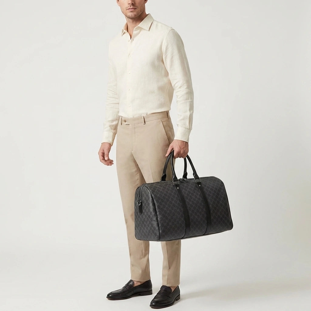 Sac de voyage homme gris damier porté à la main par les poignées, mannequin en chemise crème et pantalon beige