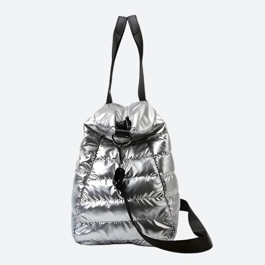 Sac de voyage matelassé argenté grand format souple avec poignées noires et bandoulière amovible sur fond uni
