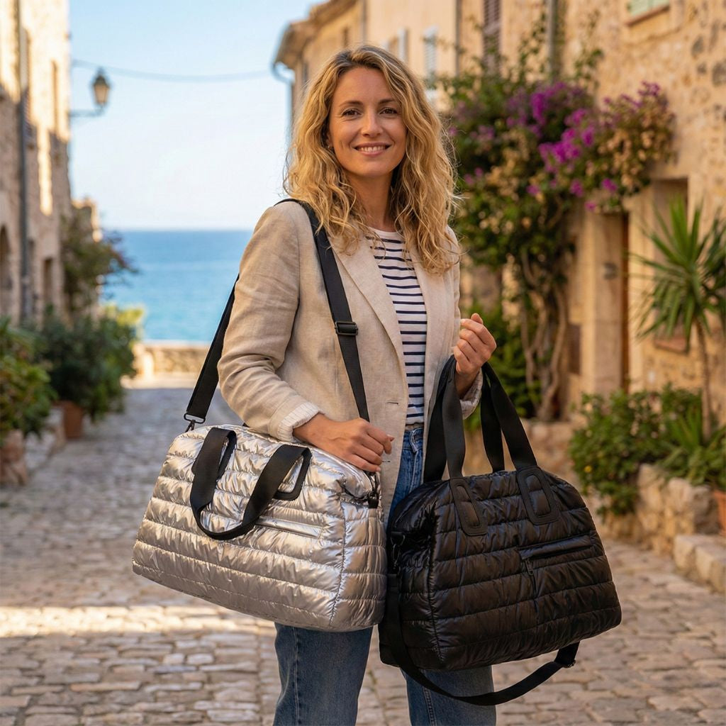 Deux sacs de voyage matelassés grand format souples, noir et argent, à bandoulière amovible portés par une femme dans une rue pavée Image