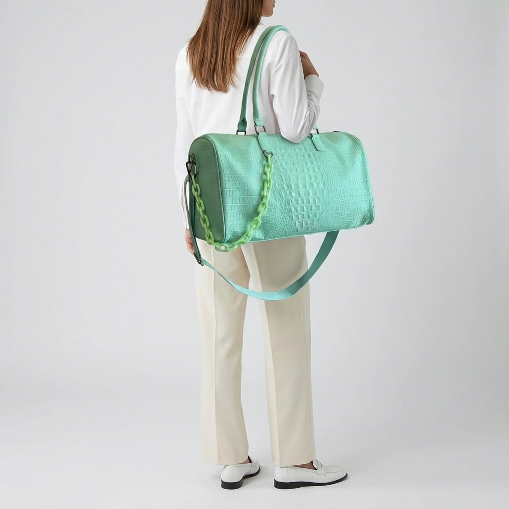 Sac de voyage vert émeraude motif croco porté en bandoulière sur l'épaule par une femme de dos