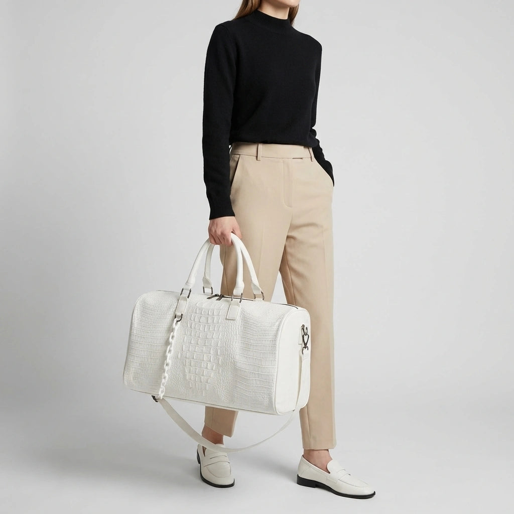 Sac de voyage blanc croco porté par une femme en pull noir et pantalon beige, look décontracté chic