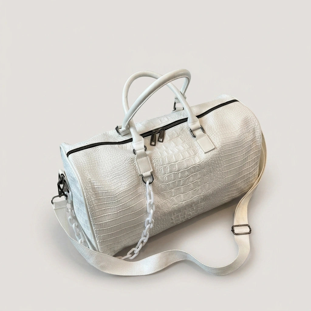 Sac de voyage blanc motif croco cylindrique posé en studio, vue 3/4 avec chaîne blanche et bandoulière