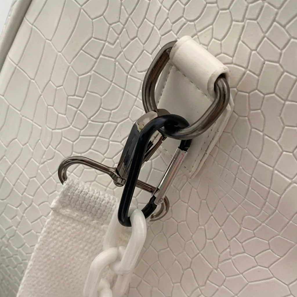 Gros plan sur le mousqueton métallique d'un sac de voyage blanc croco, fixation robuste de la bandoulière
