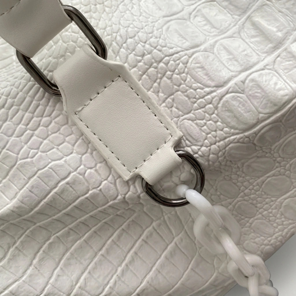 Gros plan sur la texture croco blanche d'un sac de voyage, avec l'anneau de fixation de la poignée