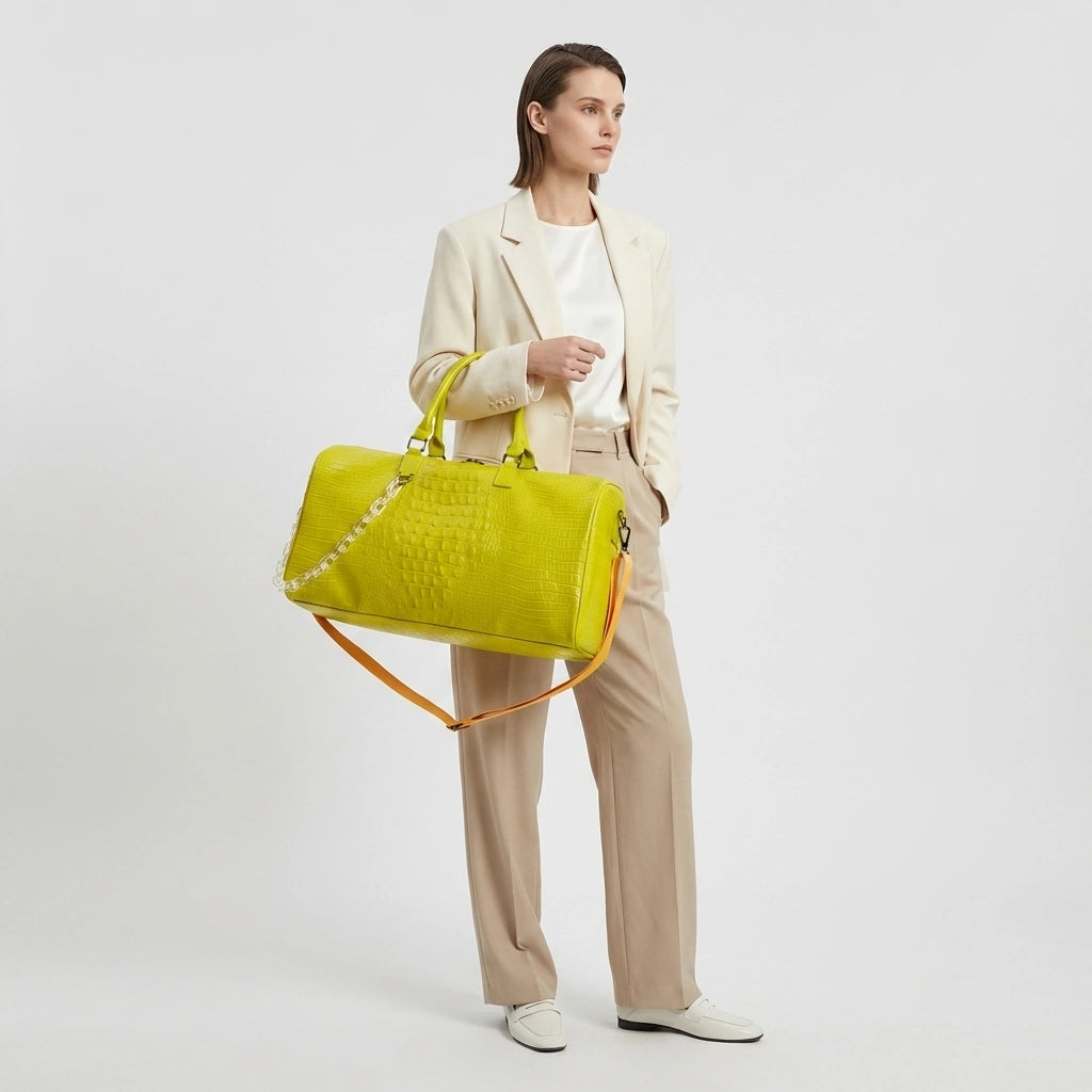 Sac de voyage vert citron motif croco tenu par les poignées, mannequin en blazer beige et pantalon clair Image