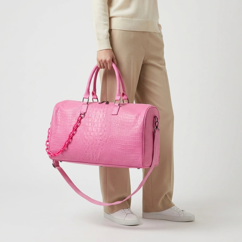 Sac de voyage rose croco saisi à la main par un mannequin en pantalon crème et baskets blanches