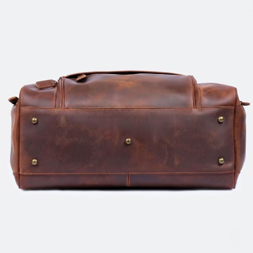 Dessous du sac de voyage en cuir marron cognac, semelle renforcée avec quatre rivets protecteurs en laiton doré
