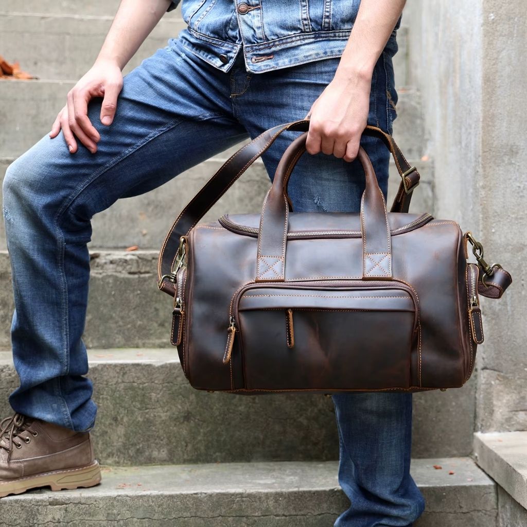 Homme assis sur des marches tenant un sac de voyage en cuir marron vintage aux garnitures dorées Image