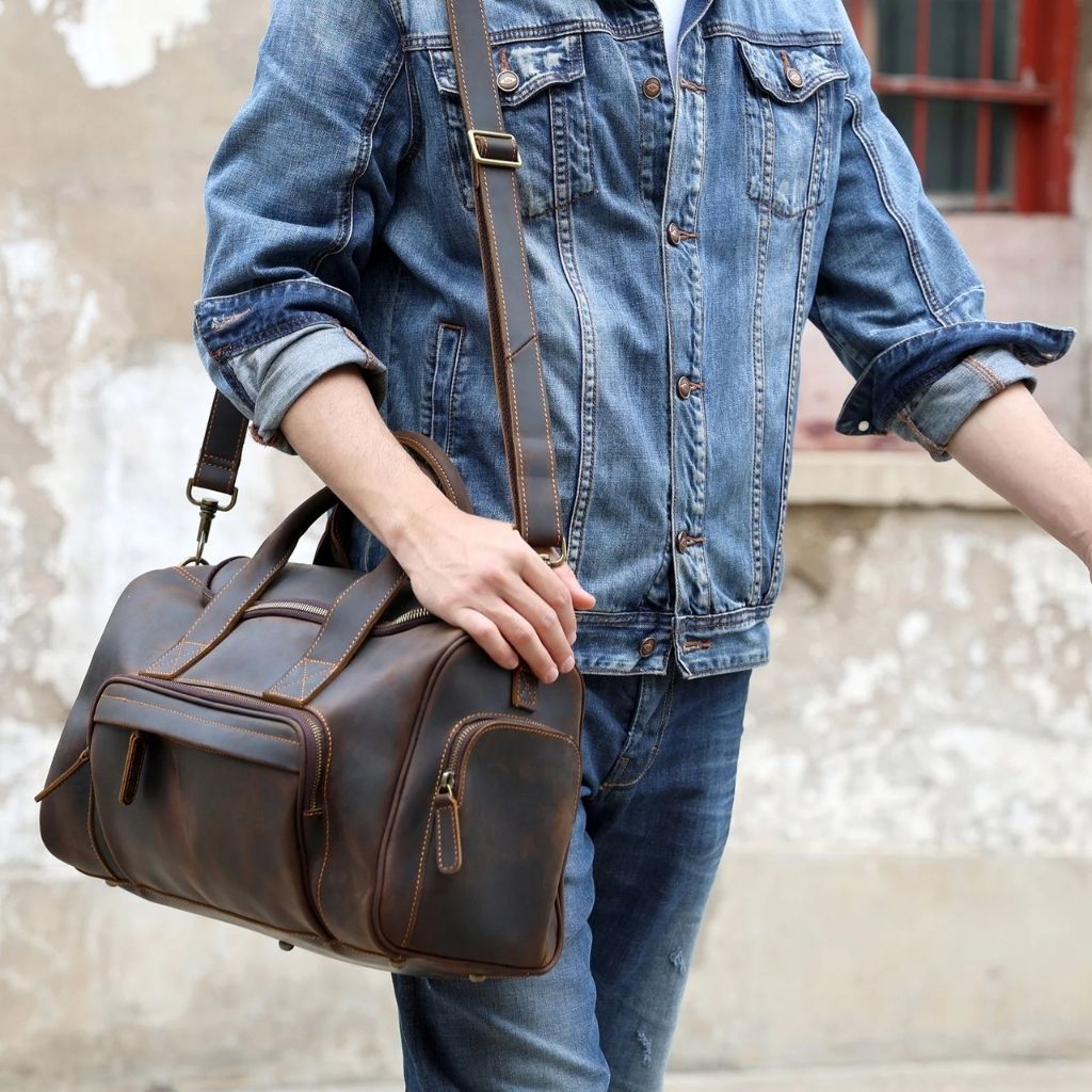 Homme en veste en jean portant en bandoulière un sac de voyage en cuir vintage marron foncé à poches Image