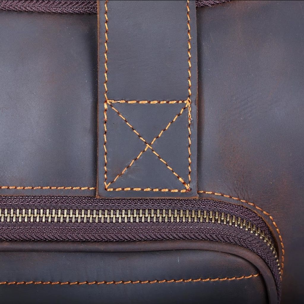 Détail du renfort de poignée du sac de voyage en cuir marron foncé, couture en croix robuste et caractéristique