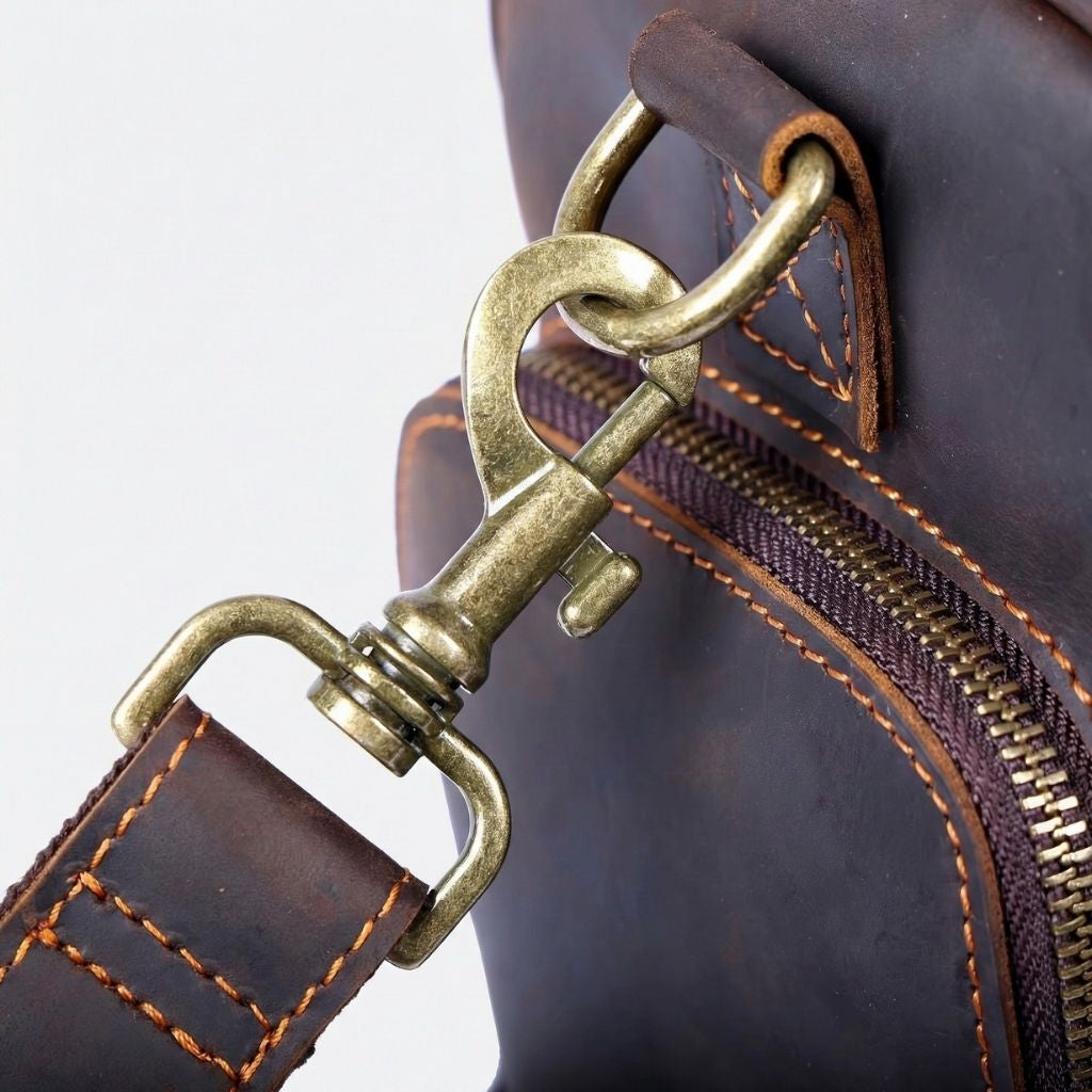 Détail du mousqueton en laiton vieilli doré du sac de voyage en cuir marron foncé, fixation de bandoulière robuste