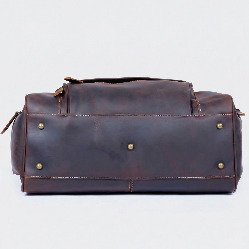 Dessous du sac de voyage en cuir marron foncé, semelle renforcée avec cinq pieds protecteurs en laiton doré