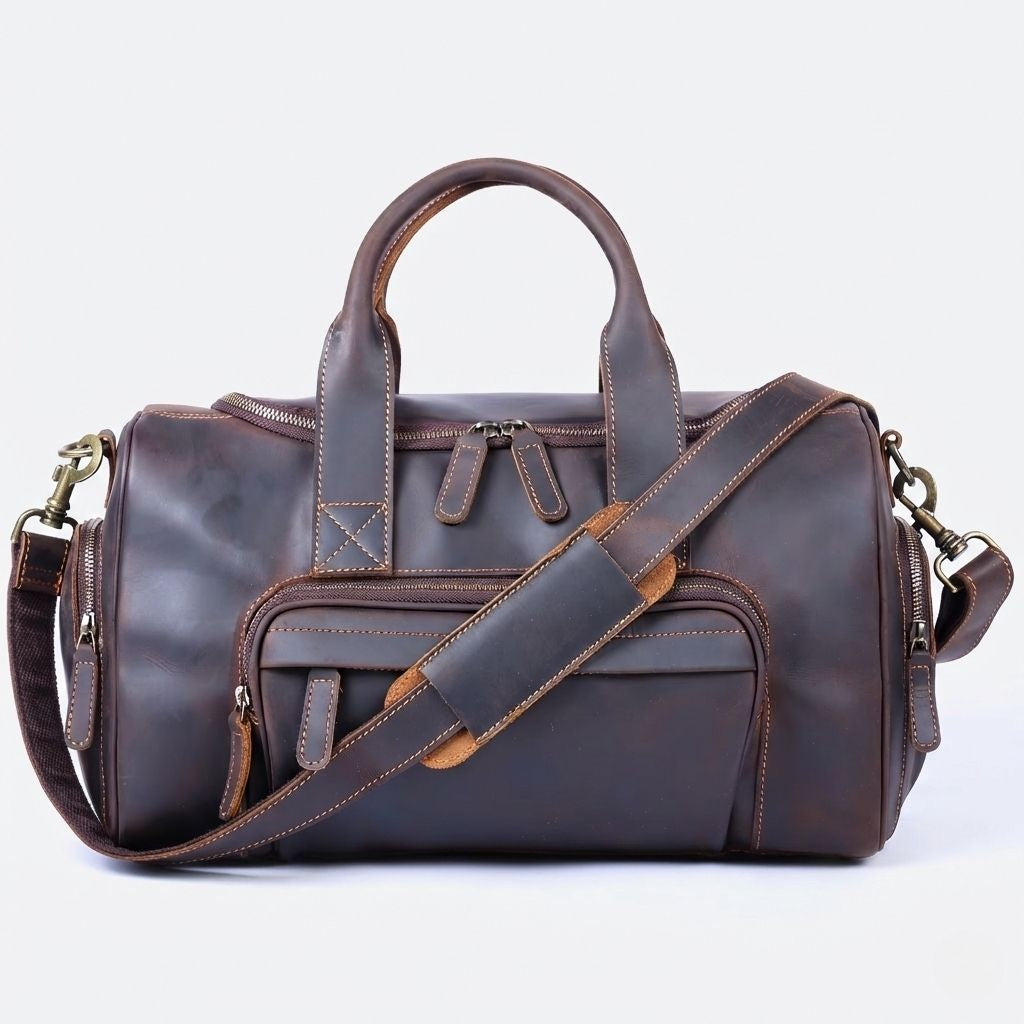 Sac de voyage en cuir marron foncé vu de face, large poche frontale zippée, double poignée et bandoulière caramel