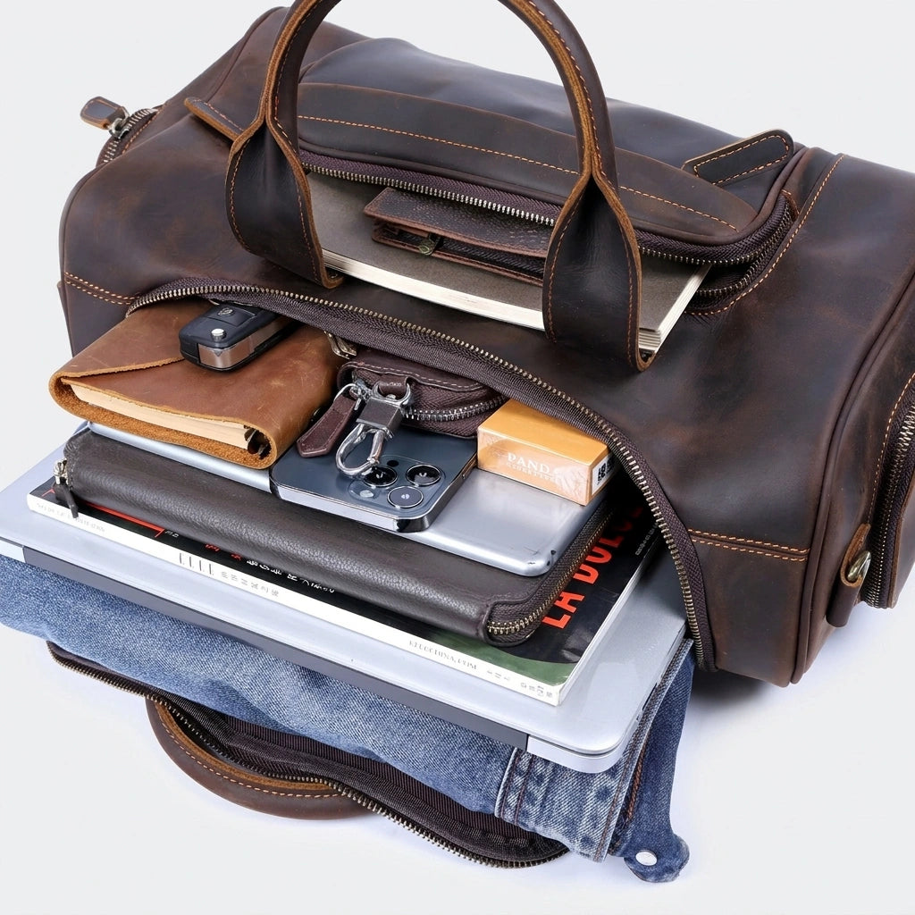 Sac de voyage en cuir marron cognac ouvert en vue 3/4, révélant l'ordinateur, le jean et les accessoires rangés