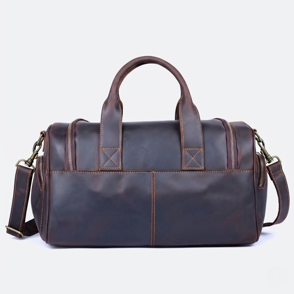 Dos lisse du sac de voyage en cuir marron foncé, coutures contrastées dorées et deux poignées courtes en arc