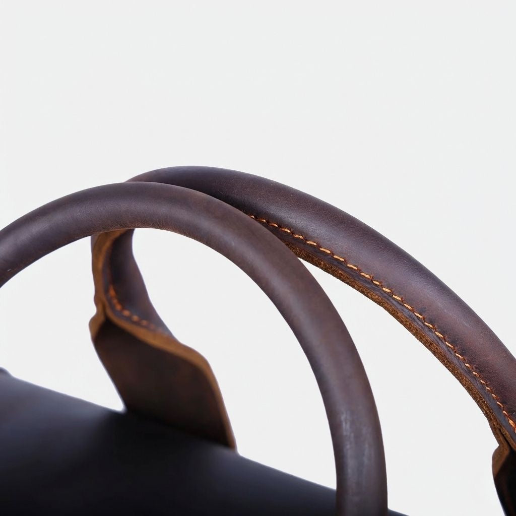 Détail des poignées du sac de voyage en cuir marron foncé, anse ronde et coutures contrastées dorées