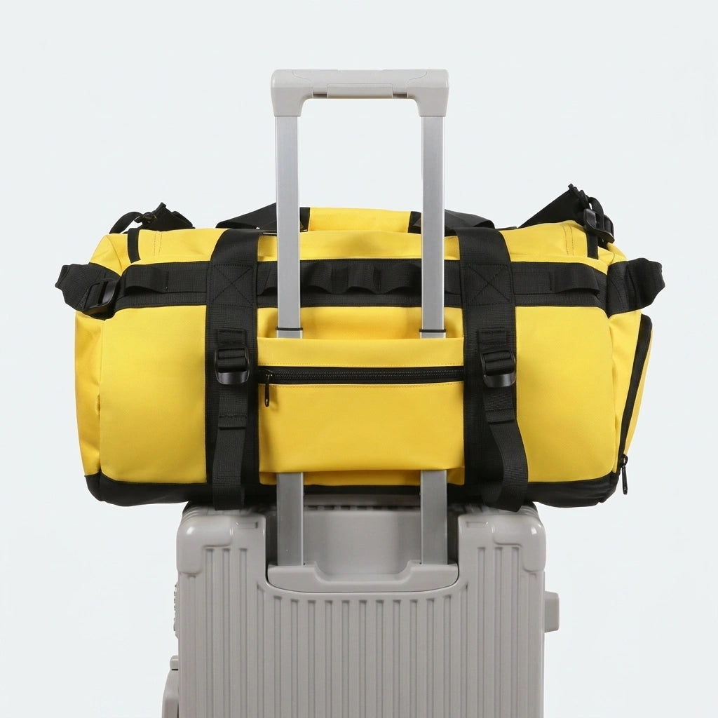 Sac de voyage jaune posé sur une valise à roulettes grise grâce à la sangle de fixation trolley