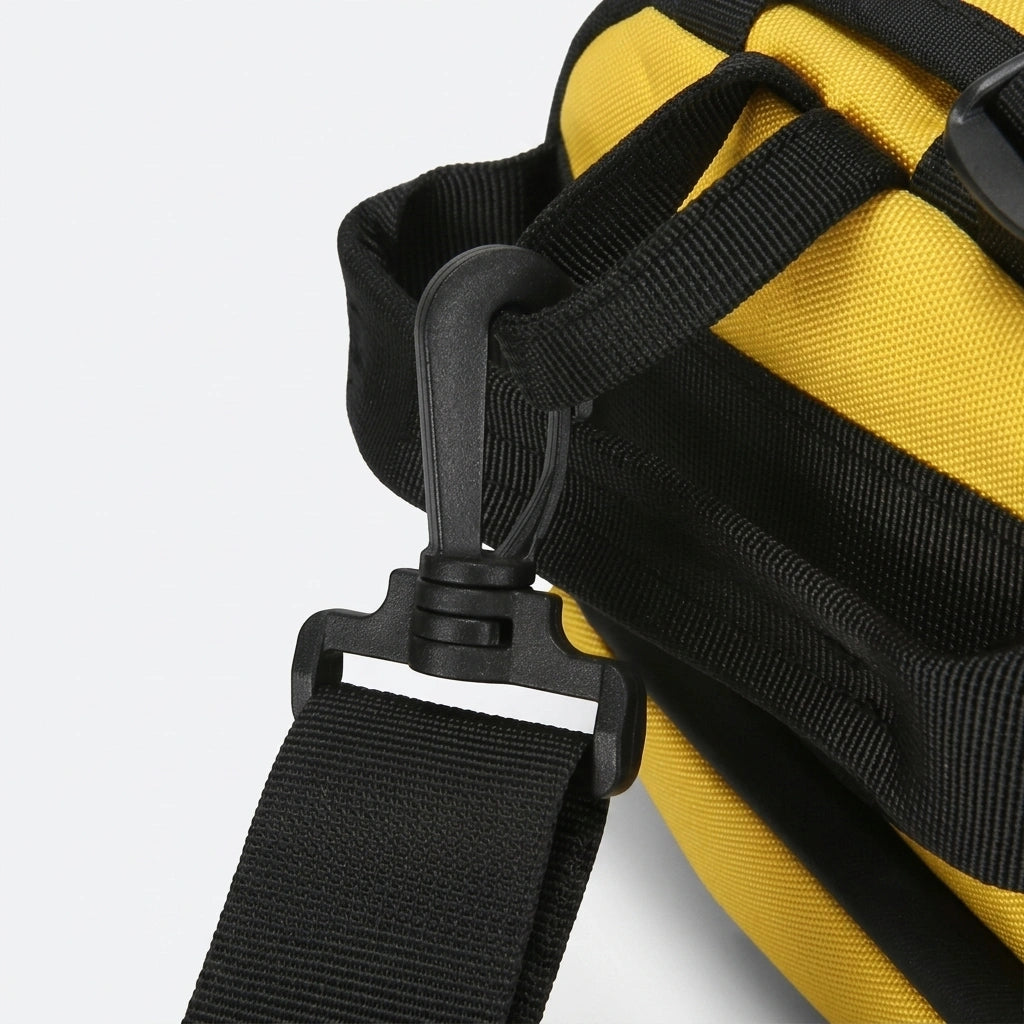 Détail du mousqueton pivotant noir fixant la bandoulière amovible et réglable sur le sac de voyage jaune